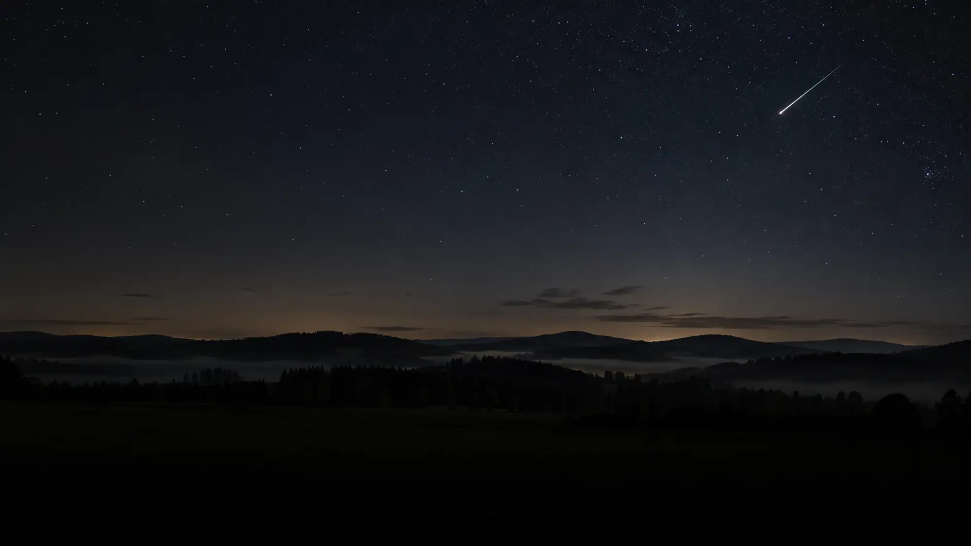 Jasná stopa meteoru na hvězdné noční obloze nad tmavou krajinou