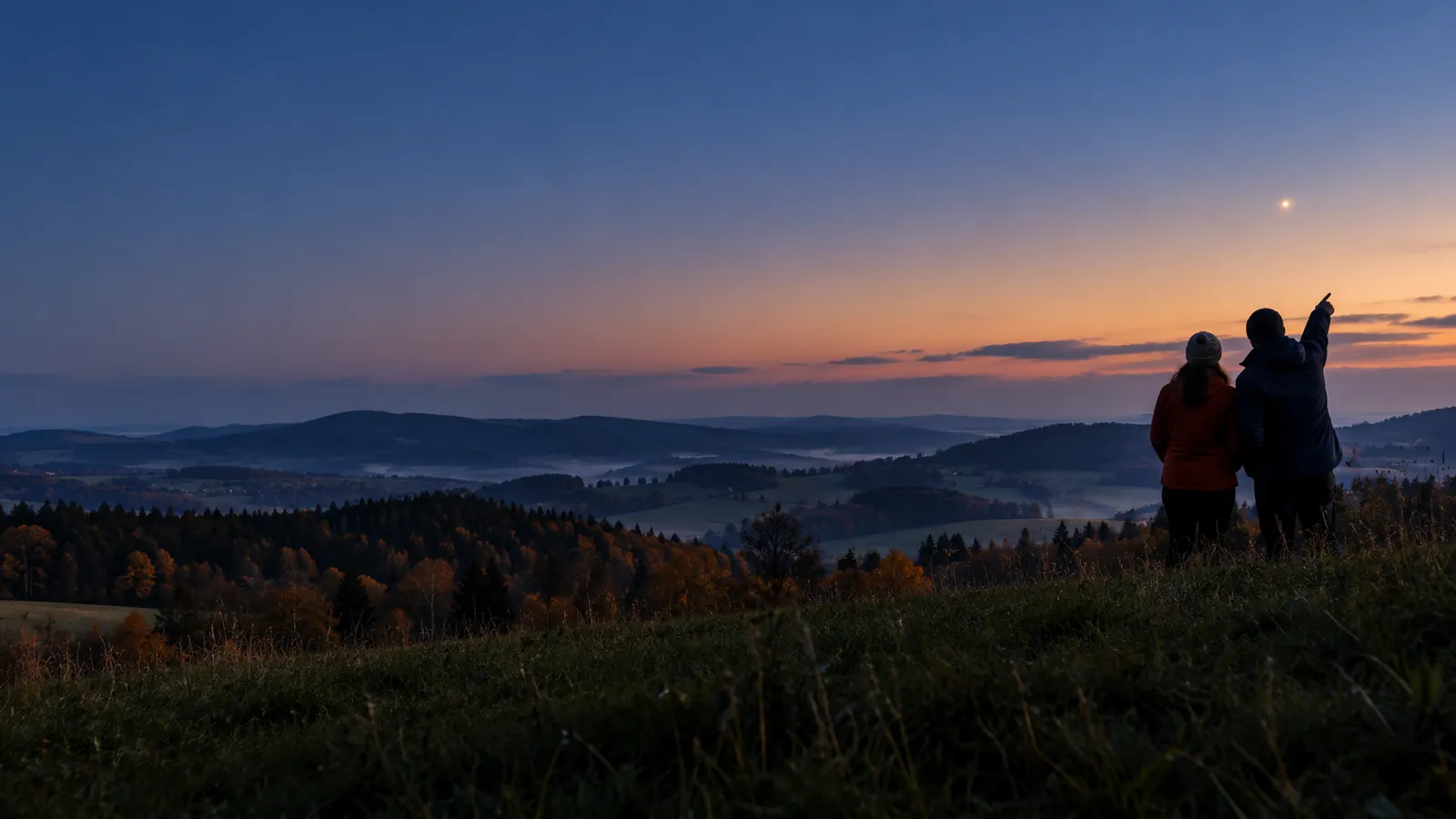 Dvě postavy na kopci za soumraku sledují nad východním obzorem jasný zlatavý bod, planetu Saturn.