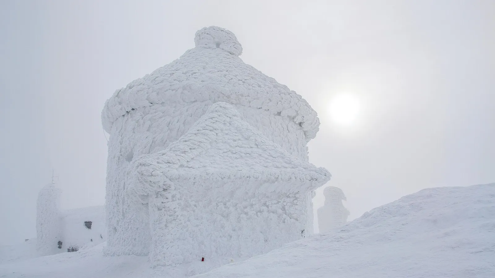 Zasněžený vrchol Sněžky v Krkonoších s kaplí a budovou observatoře.
