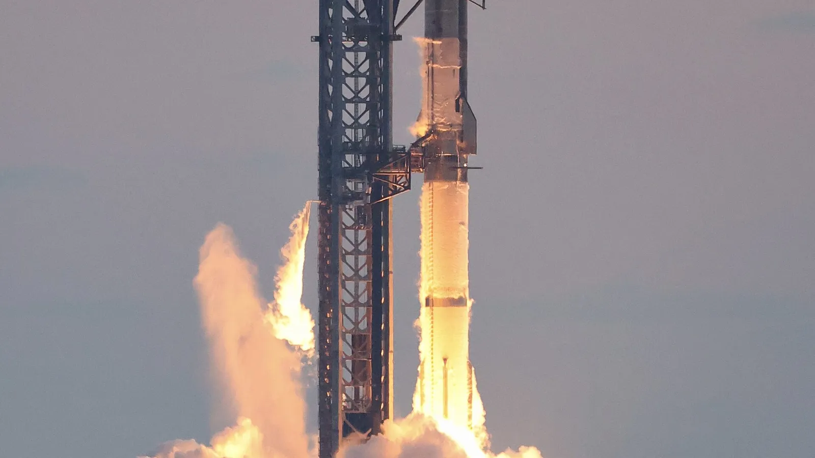 Raketa Starship startuje z rampy, pod ní plameny a oblaka kouře.